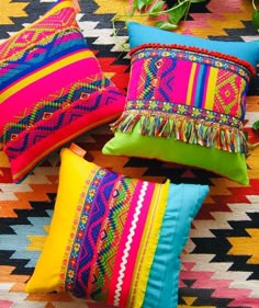 brightly colored pillows are arranged on a colorful rug with greenery in the back ground