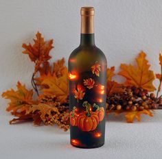 a wine bottle decorated with pumpkins and lights on the label is sitting in front of some autumn leaves