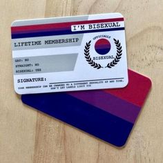 two credit cards sitting next to each other on top of a wooden table and one has a red, purple, and blue stripe around it