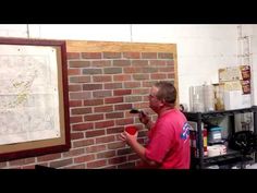 a man standing in front of a brick wall holding a paint roller and looking at a map