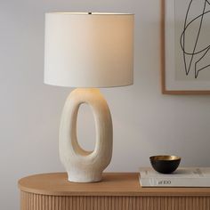 a table lamp sitting on top of a wooden dresser next to a book and bowl