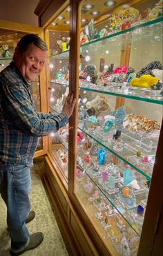 a man is looking at the glass shelves with many items in it and smiling for the camera