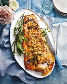 a white plate topped with fish next to a knife and flowers on top of a blue table cloth