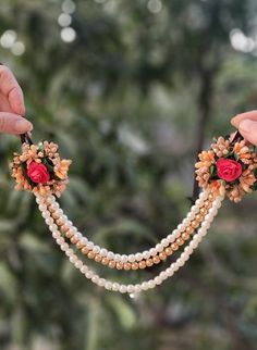 two hands holding necklaces with flowers and pearls