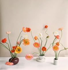 three vases with flowers in them sitting on a table next to a white wall