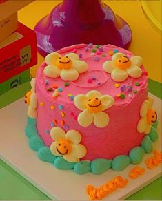 a pink cake with flowers and smiley faces on it sitting next to a stack of books