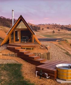 a small wooden cabin with a hot tub in the foreground and steps leading up to it