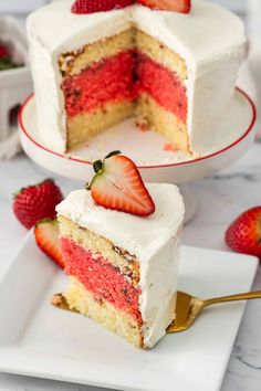 a slice of strawberry cake with white frosting and strawberries on the side, ready to be eaten