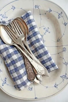 two forks and spoons are sitting on a blue and white checkered cloth napkin