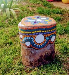 a colorfully painted box sitting on top of a tree stump in the middle of grass