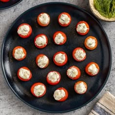 an overhead view of mini tomatoes with cream cheese on them, sitting on a black plate