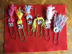 some paper clips with eyes and hair on them are sitting on a red cloth covered table