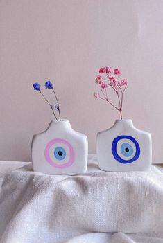 two ceramic vases with blue and pink designs on them sitting on a white sheet