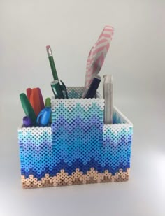 a pen holder made out of perforated paper and plastic material with pens, markers, scissors and pencils in it