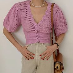 a woman with her hands on her hips wearing shorts and a pink sweater, holding a purse