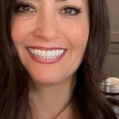 a woman with long dark hair smiling at the camera, wearing a necklace and white shirt