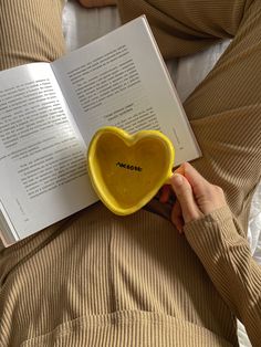 a person reading a book while holding a yellow heart shaped bowl