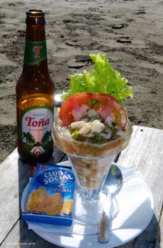 there is a salad in a glass on the table next to a bottle of beer