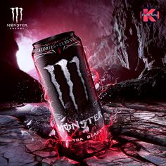 a can of monster energy drink sitting on top of a rock covered ground with red light coming from it