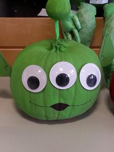 a green pumpkin with googly eyes sitting on top of a counter next to an apple