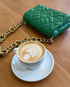 a cappuccino on a saucer with a green purse behind it