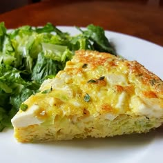 a white plate topped with a slice of quiche next to a green leafy salad