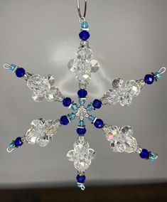 a snowflake with blue and white beads hanging from it's side in front of a gray background