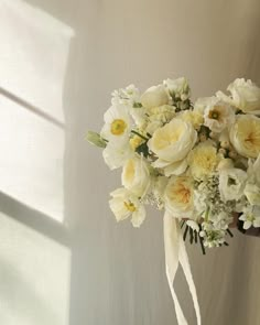 a bridal bouquet with white and yellow flowers in the foreground, against a light colored wall