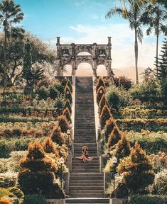 a woman sitting on top of a set of stairs in the middle of a garden