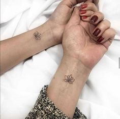 two hands holding each other with small tattoos on their wrists and wristbands, one has a lotus tattoo on it