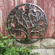 a metal tree with leaves on it hanging from a red wooden wall next to green plants