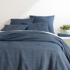 a bed with blue linens and pillows in a white room next to a potted plant