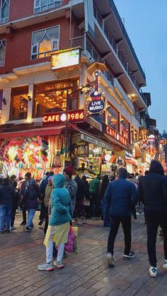 many people are walking around in front of a building at night with christmas lights on