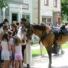 a group of people standing next to a brown horse on a sidewalk near a building