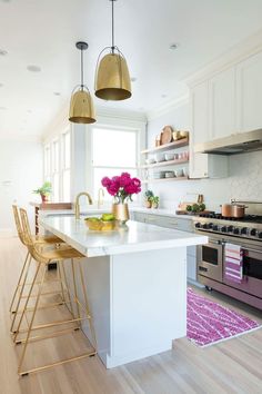 a white kitchen with gold accents and brass bar stools in front of the island