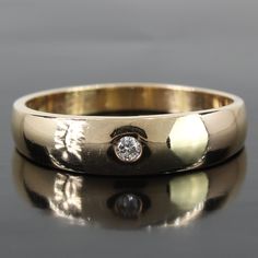 a yellow gold wedding band with a diamond in the center, on a reflective surface