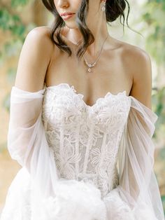 a woman wearing a white dress and holding a flower in her right hand, looking off to the side