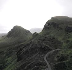 a winding road in the middle of some mountains with green grass on both sides and a hill behind it