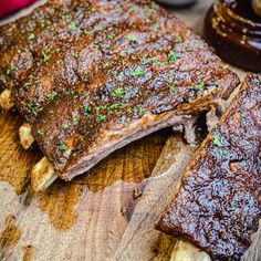 a close up of ribs on a cutting board with sauce and seasoning next to it