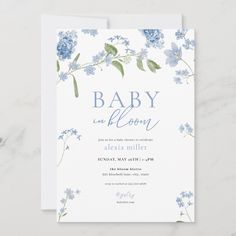 a baby shower card with blue flowers and greenery on the bottom, in front of a white background