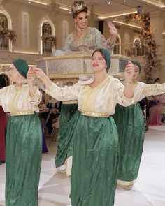 three women dressed in green and white are dancing with their hands up to the sky