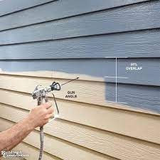 a man spray painting the side of a house with blue siding and white paint on it