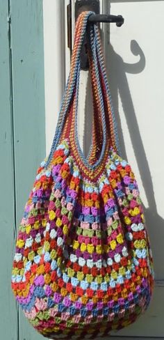 a multicolored crocheted purse hanging from a hook on a white door