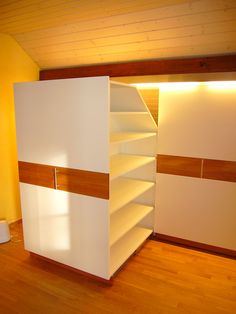 an empty room with white shelves and wood flooring on the walls, in front of a yellow wall