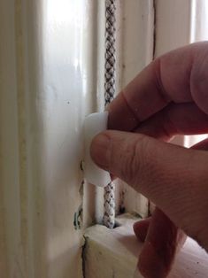 a hand is holding an object in front of a window frame that has been stripped off