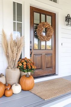 two pumpkins are sitting on the front porch next to a wreath and some flowers