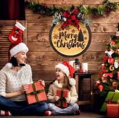 two women sitting on the floor with presents in front of christmas decorations and a wooden wall