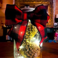 a mason jar filled with pine cones and christmas lights is adorned with a red bow