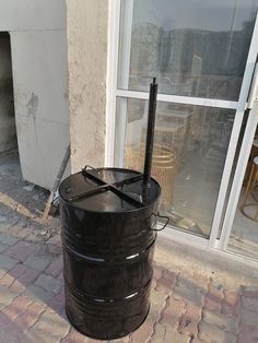 a large black barrel sitting on top of a brick sidewalk next to a building with a window