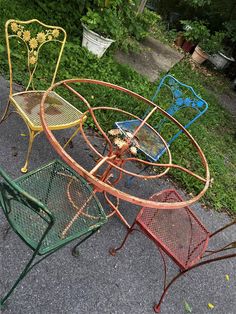 three metal chairs sitting next to each other on top of a cement ground in front of bushes